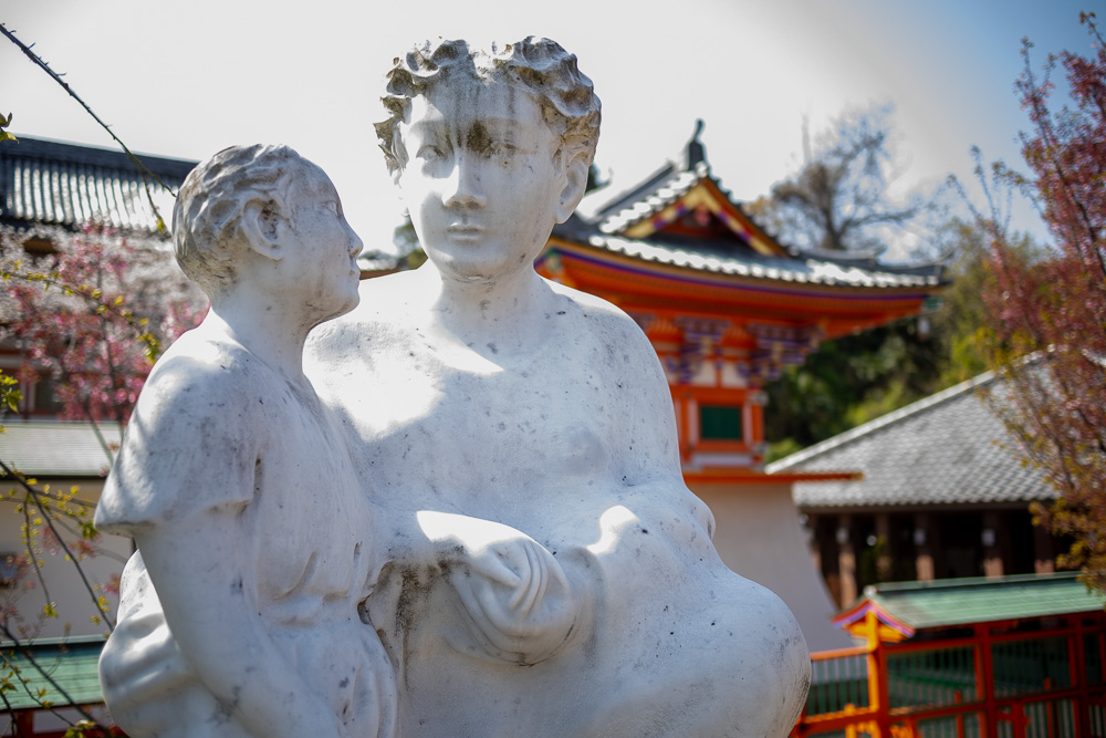 Marble statue of a woman and child in front of an orange temple.